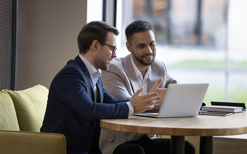 Two men discussing behind a laptop