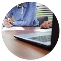 Man with pen and paper in front of laptop computer 