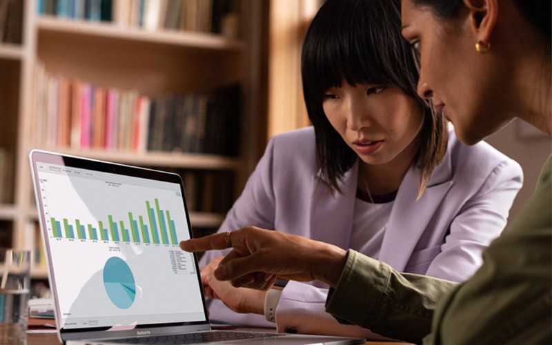 Designed to work seamlessly with iPhone and iPad Two colleagues sharing a MacBook in a meeting