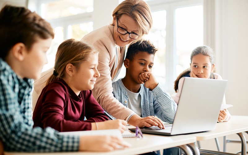 Teacher helping young students with a laptop