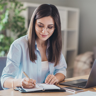 woman writing in notebook by surface laptop