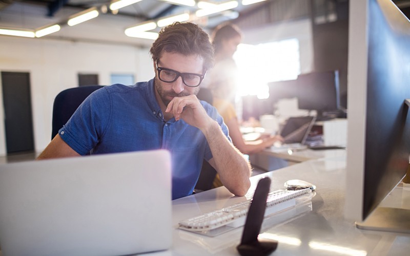 Businessman on desktop and laptop device in open office