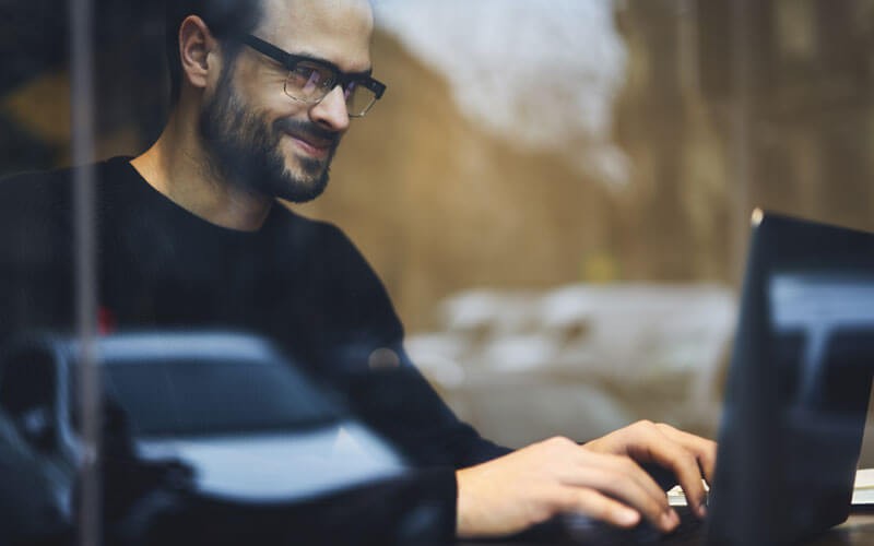 business-man-working-remoteley-smiling-at-laptop business-man-working-remoteley-smiling-at-laptop