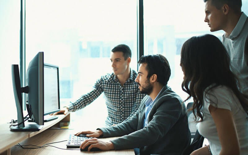 Group of IT professionals gather around desktop computer in front of window