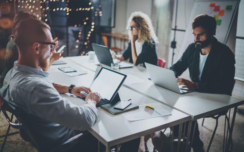Group of colleagues working late on devices in office at night