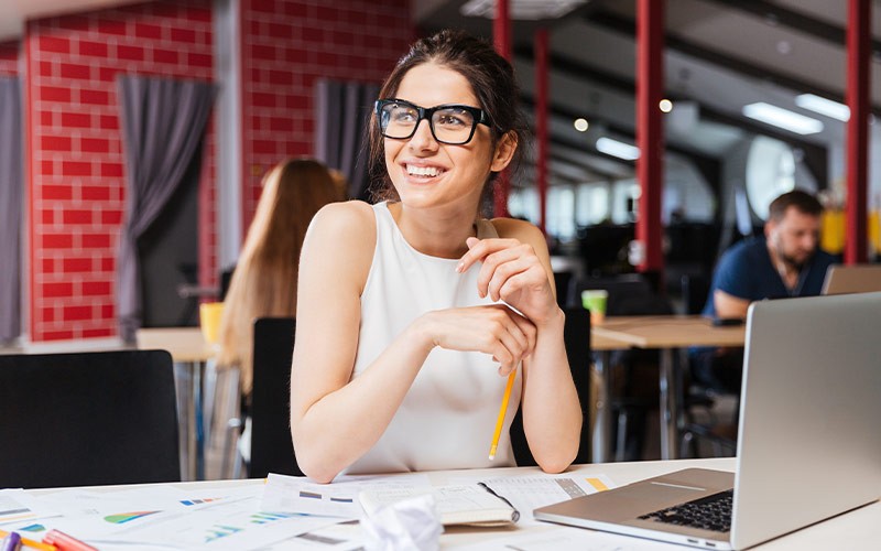 Woman smiling in front of a laptop while looking at a colleague