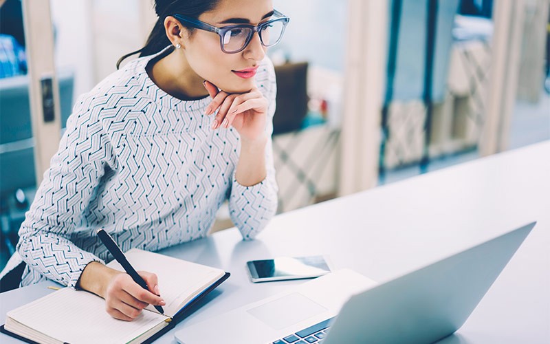 Woman taking notes while working on a laptop